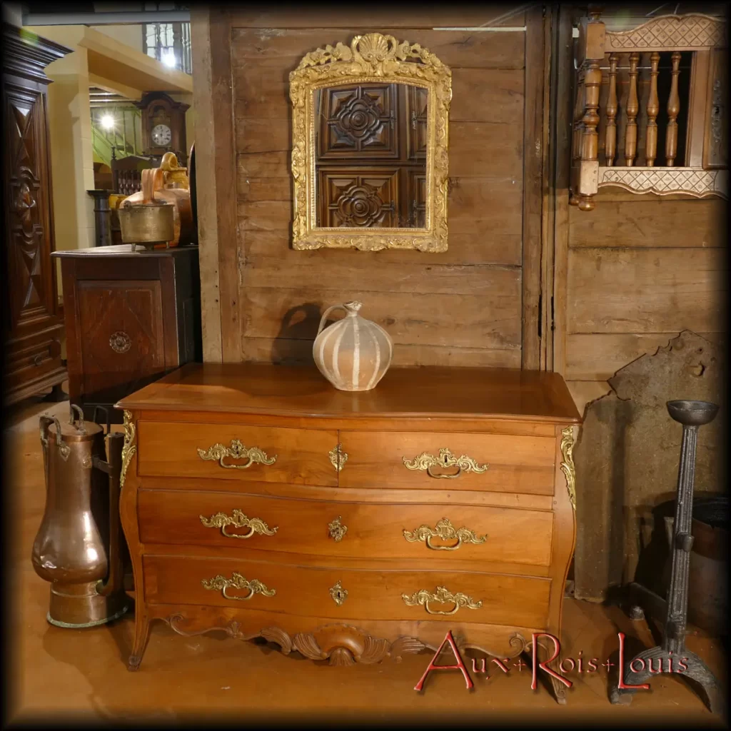 Galbée sur la façade et sur les côtés, cette commode Rocaille en noyer blond Louis XV conjugue chic et élégance. Tout ici est douceur, rondeur et féminité. En haut des montants, des chutes de bronze en feuilles d’acanthe répondent aux mêmes motifs sculptés dans le noyer sur la traverse du bas, qui par ailleurs porte en son sein une coquille Saint-Jacques délicatement ouvragée.